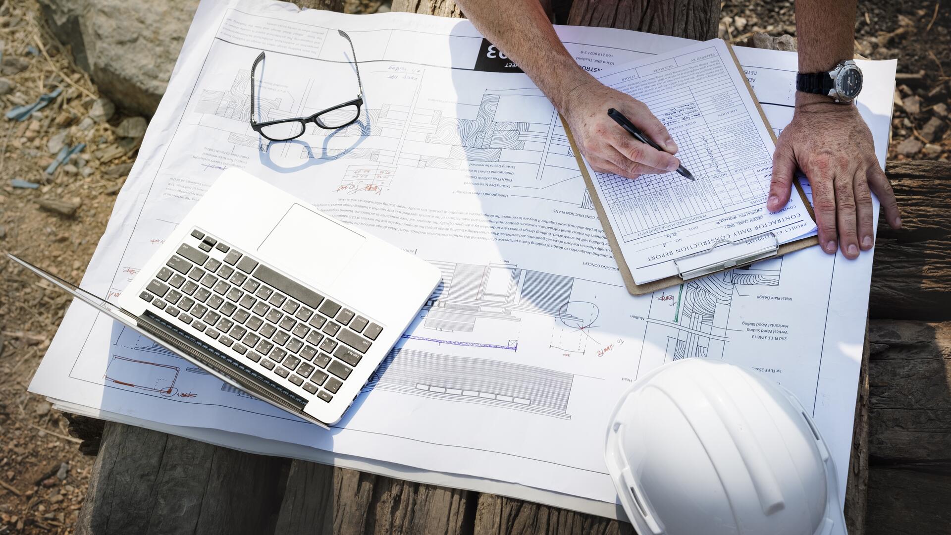 Engineering surveyor reviewing construction site plans with laptop on timber bench